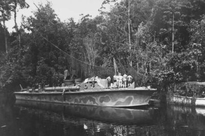 PT-66 sits moored at the Morobe PT boat base in 1943. The vessel’s camouflage paint scheme helped it blend with the shoreline. Camouflage netting strung among the trees in the background added further concealment from enemy aircraft.