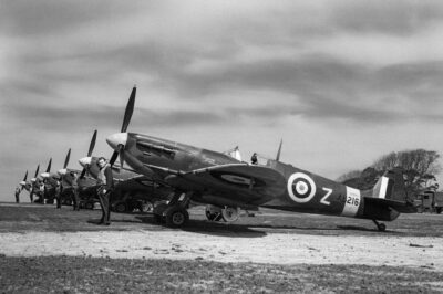 Spitfire Mk Vs of No. 91 Squadron lined up at Hawkinge, May 1942. Standing nearest the camera is the Squadron’s Commanding Officer, Squadron Leader R. W. Oxspring, in front of his personal aircraft, a Mark VC, AB216 DL-Z. Next to him, in front of another Mark VC, is the ‘B’ Flight commander, Flight-Lieutenant F. H. Silk. The remaining aircraft are Mark VBs.