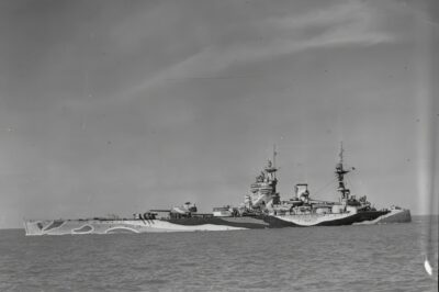 This photo shows the HMS Rodney, a Nelson-class battleship of the Royal Navy, in her wartime dazzle camouflage. The design concentrated all three 16-inch gun turrets forward, giving her a unique profile. Rodney wore disruptive paint patterns like this to break up her outline at sea. Though considered slow and unconventional in appearance, she proved decisive in action—most famously in May 1941, when she helped destroy the German battleship Bismarck.