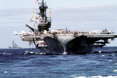 A bow view of the aircraft carrier USS Midway (CV-41) sailing in the wake of the battleship USS Iowa (BB-61). The frigate USS Francis Hammond (FF-1067) is off the Midway’s port side, December 1987.