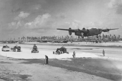 A U.S. Army Air Forces B-24 Liberator lifts off from Eniwetok Island, April 1944, while Navy Seabees spread coral to widen the airstrip. These forward bases gave Allied bombers reach deep into Japanese-held territory. The crushed coral runways of Pacific islands often turned to choking dust clouds under heavy bomber traffic, coating engines and equipment.